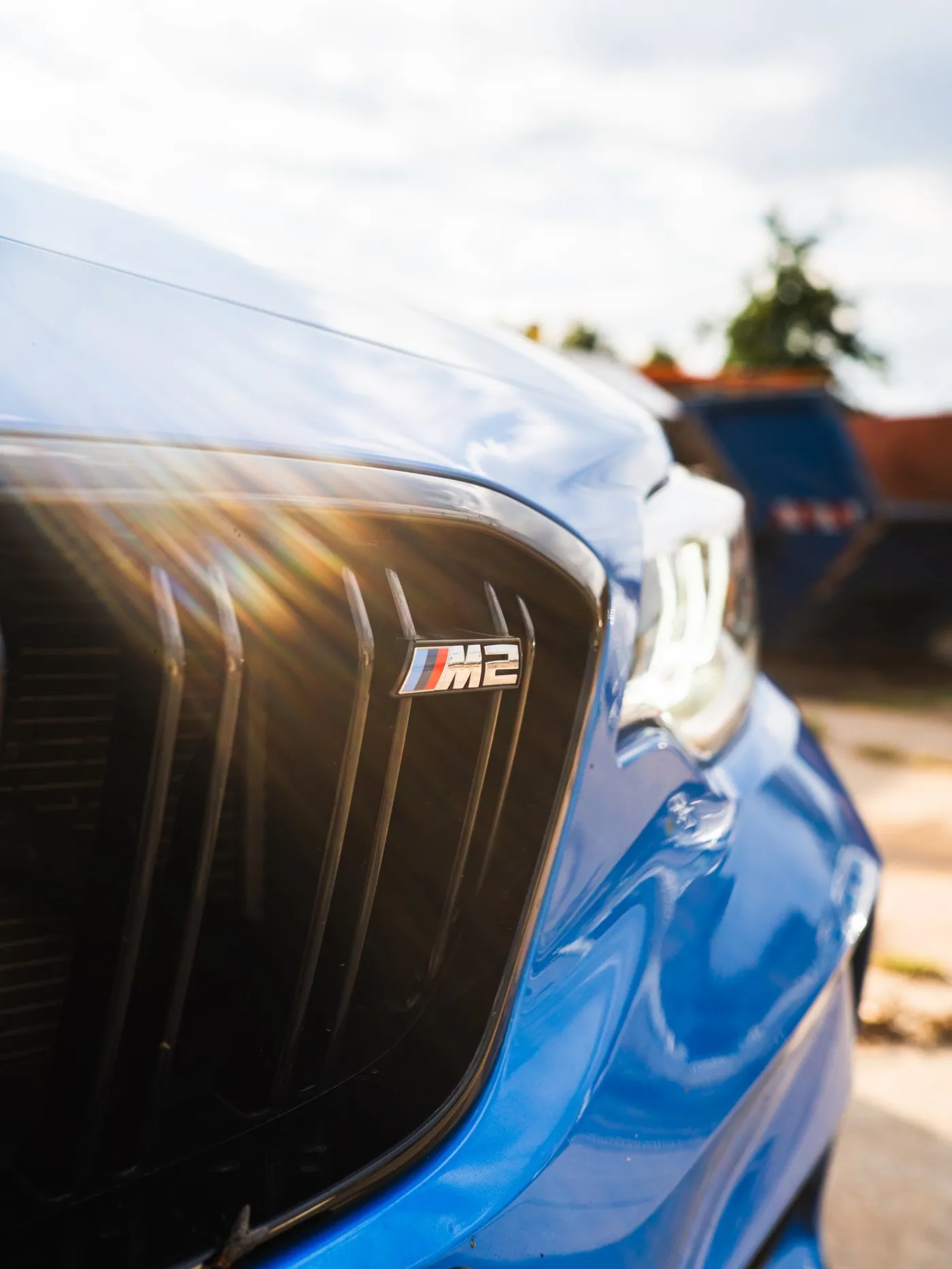 Kühlergrill eines blauen BMW M2 mit M2-Emblem im Gegenlicht